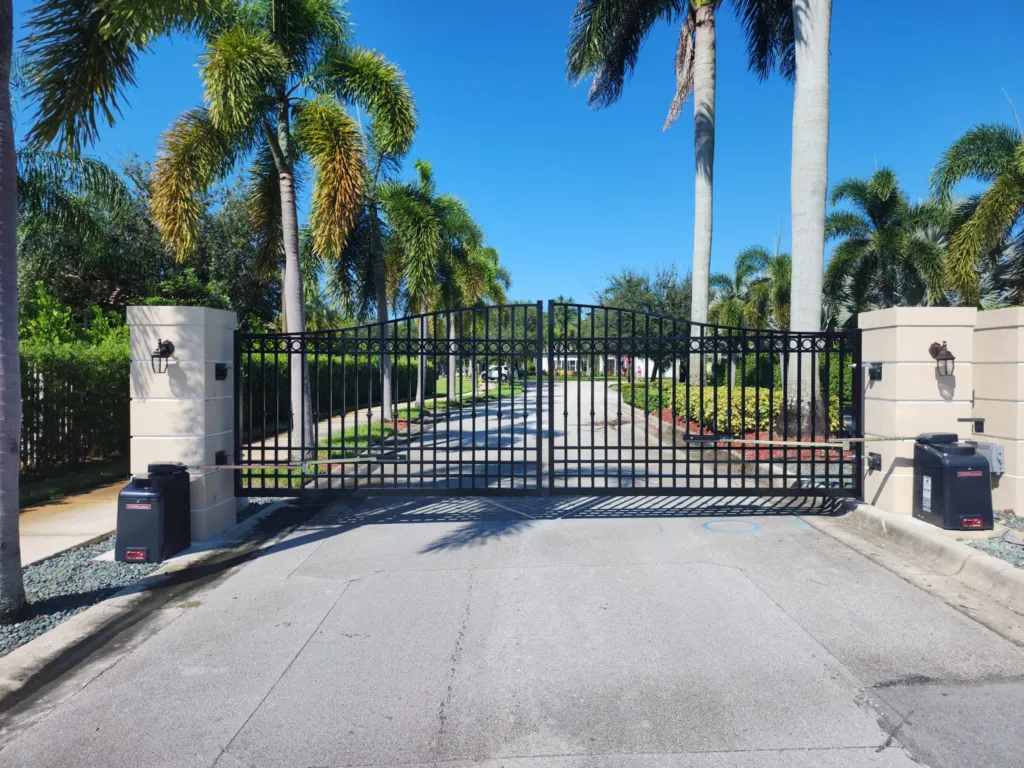 Black iron double swing gate with two gate operators on a palm-lined private road